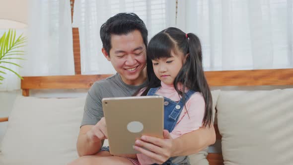 Asian loving father with little girl using tablet learning from home and playing internet online. alt