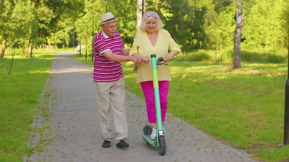 Senior Old Stylish Tourists Grandmother Grandfather Using Electric Scooter While Riding in Park alt