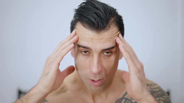 Headshot of Young Overwhelmed Man Rubbing Temples Looking at Camera with Brown Eyes alt