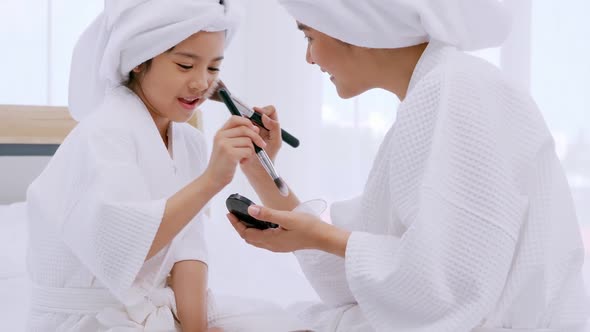 Mother with little daughter in bathrobes doing beauty treatment together at home. alt