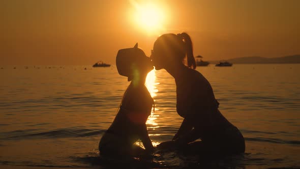 Silhouettes Mother and Daughter Sit on the Beach at Sunset. Concept of Friendly Family, Lifestyle alt