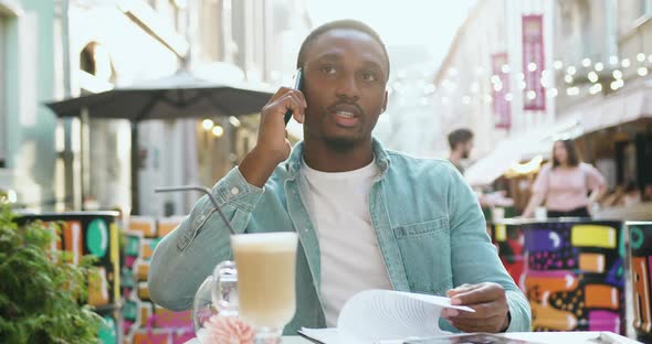Office Worker Talking on Mobile while Working with Financial Documents in Cozy Street Cafe alt