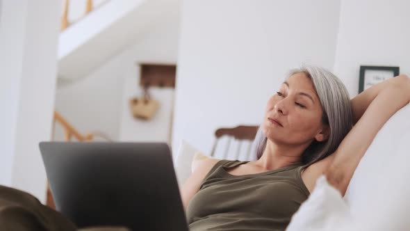 Dreaming Asian woman thinking and looking at laptop alt