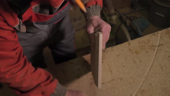 Carpenter Stands Behind the Workplace Polishes with Sandpaper Processes Wood alt