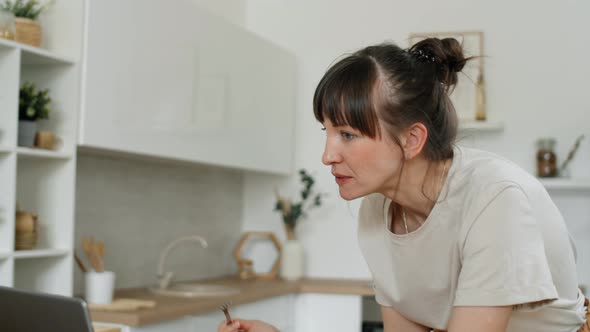 Woman Eating Salad and Browsing the Web on Laptop in Kitchen alt