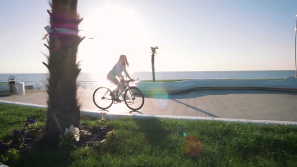 Young Stylish Woman Cyclist Enjoying Fixed Gear Bike Riding Outdoors at Sunrise Near the Sea alt
