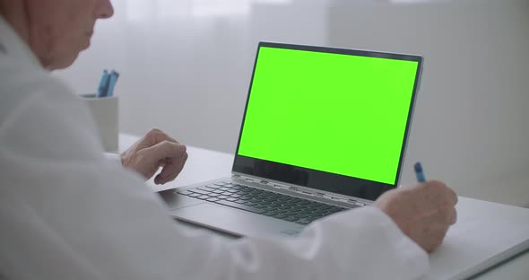 Doctor Is Looking on Laptop with Chroma Key Screen on Table in Office of Clinic, Writing Notes alt
