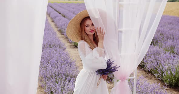 Beautiful Girl in a Hat with a Bouquet of Lavender Near the Gazebo alt
