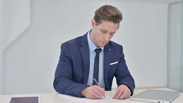 Disappointed Young Businessman Trying To Write on Paper  alt