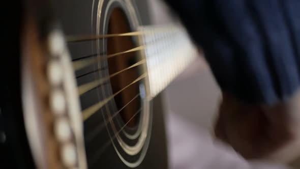 DOF A Boy's Hand Plays the Strings of a Black Acoustic Guitar