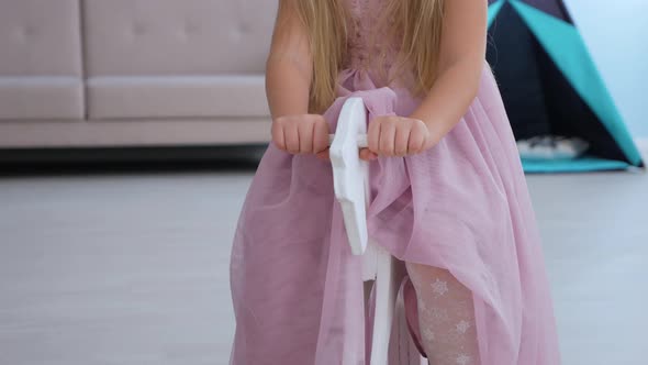 Close-up of children's hands rides toy horse. Girl in purple dress plays in room