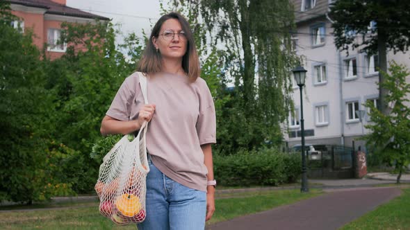 Woman walks outside with mesh string knitted shopping bag alt