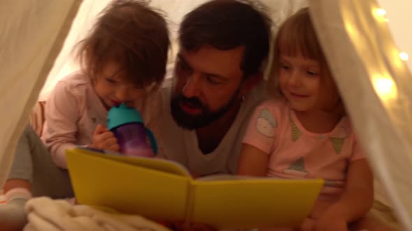 Dad and Little Daughters Reading Book in Teepee Tent