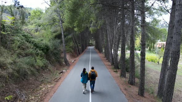 Aerial Flyover of Couple Walking on Concrete Path Through Woods alt