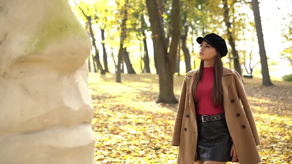 Fashion Girl in Stylish Clothes Posing at Sculpture in Sunny Autumn Park alt