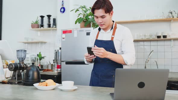 Asian businessman cafe owner take photo of cup of coffee in cafe and using laptop computer. alt