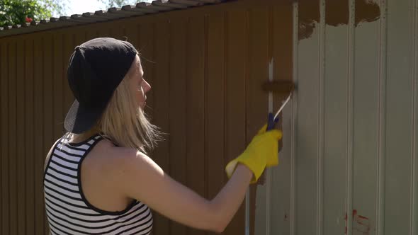 girl in a cap paints a garage with a roller outside