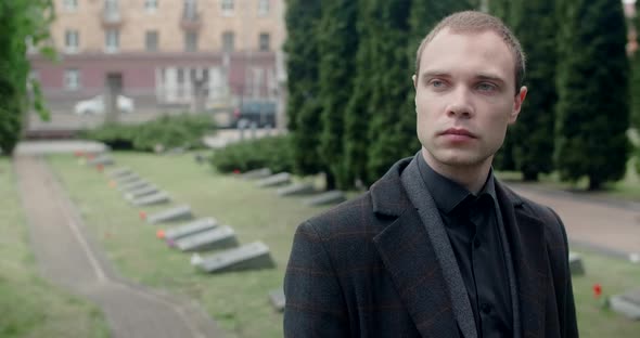 Sad Young Man in Suit and Overcoat Stands on the Cemetery