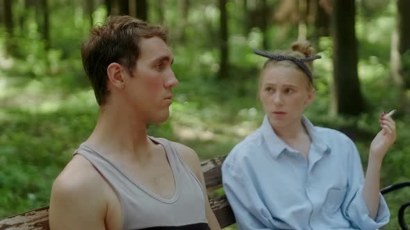 A Guy and a Girl Communicate on a Bench in the Forest alt