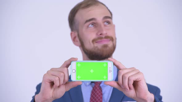 Face of Happy Bearded Businessman Thinking While Showing Phone