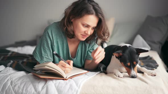 A Young Woman Is Writing a Diary While Lying in Bed with Her Basenji Dog alt