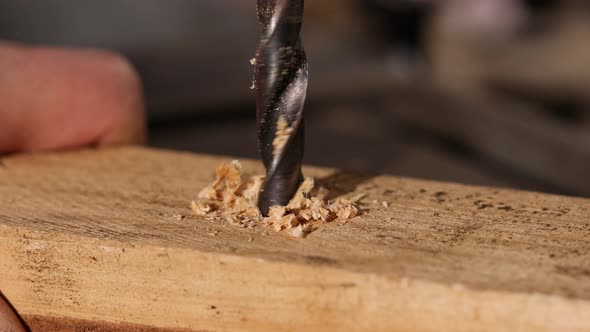 Man is drilling a hole in a piece of wood with a drill. Craft, industry, woodwork