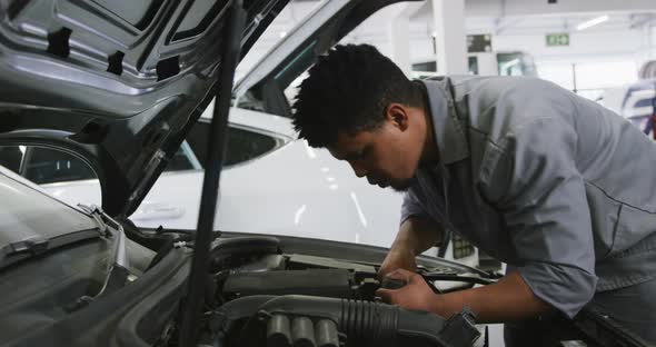 African American male car mechanic looking at an open car engine and checking if something is broken alt