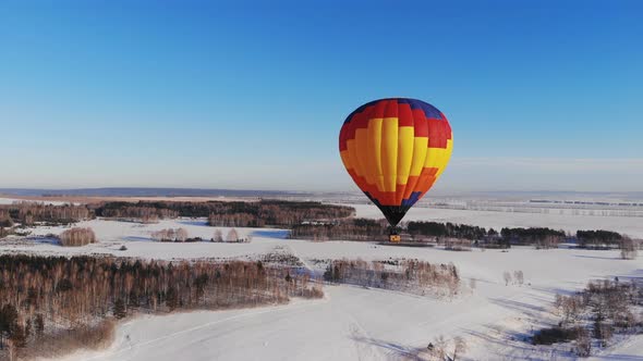 Aerial Shot of the People Fly on a Big Bright Balloon Over the Winter Forest.