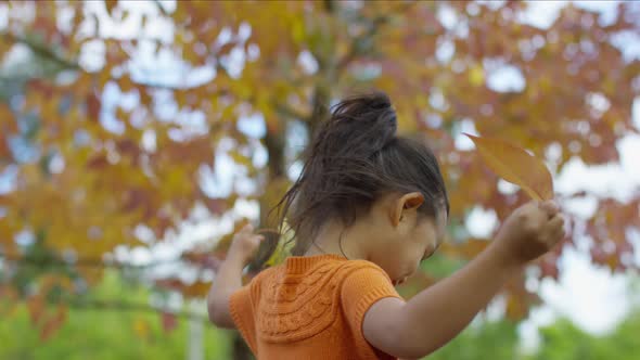 Young girl in Fall spinning with leaves in hands