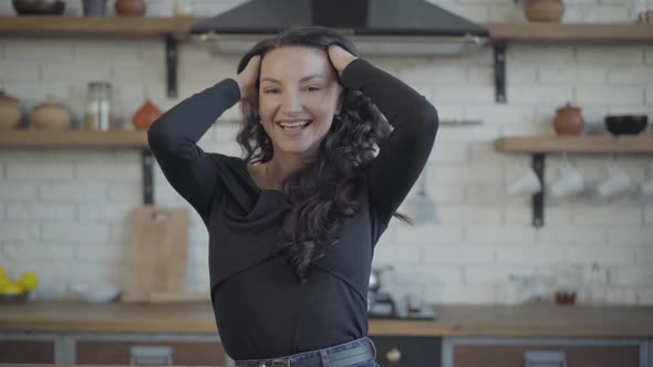 Middle Shot Portrait of Young Cheerful Caucasian Woman Winking and Smiling Holding Hands on Head alt
