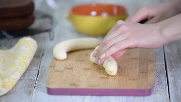 Close-up on woman cutting banana on cutting board. alt