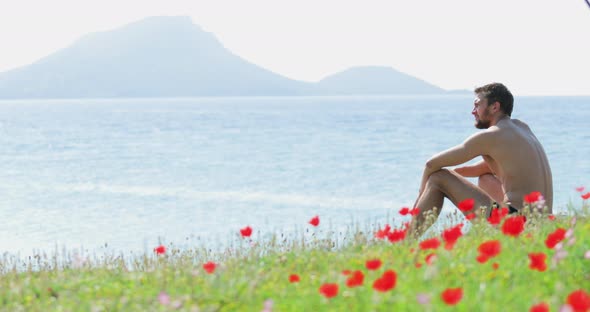 The Handsome Man Sits on a Glade Before the Sea a Lot of Flowers of Poppies Picturesque Sea alt