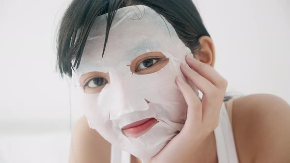 Beautiful young asian woman applying sheet facial mask for skin care and treatment. alt