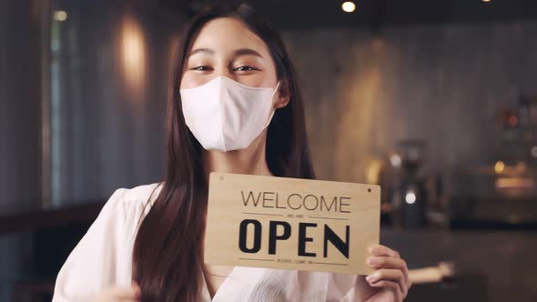 Business owner attractive young asian woman in apron hanging we're open sign alt
