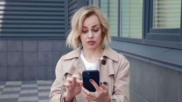 Shocked Business Woman Looking with Surprise at the Smartphone Screen and Covers Her Mouth with Her alt