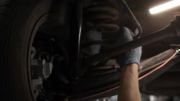 Close Up Woman Hand Mechanic in Car Servic Checks Suspension of Car That is Raised on Lift in Repair alt