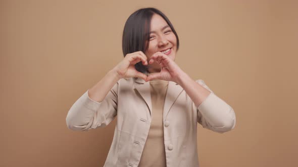 Happy asian business woman in love showing i love you sign language and looking at camera isolated