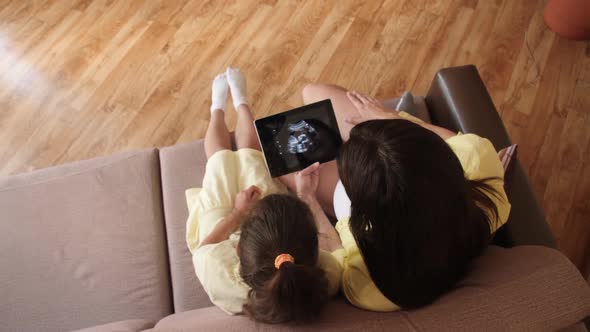 A Young Pregnant Woman with Her Daughter Is Watching an Ultrasound Video on a Tablet. Waiting 