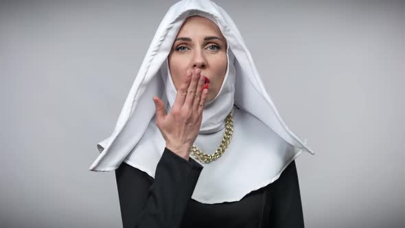 Beautiful Smiling Woman in Nun Costume Sending Air Kisses Looking at Camera Posing at Grey alt