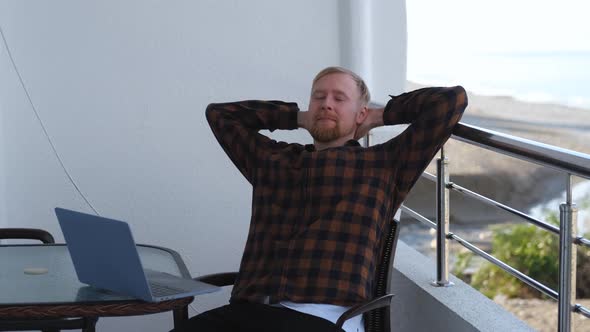 man relaxing in front of laptop sitting on hotel balcony on vacation