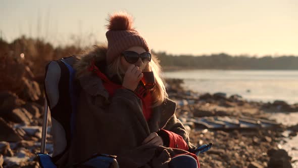 Female Drinking Hot Tea Or Coffee From Mug. Woman Warming Hands Steaming Cup Of Mate Tea. alt
