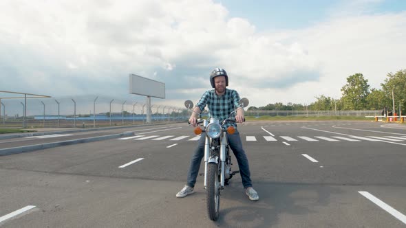 Young Man Biker with Custom Motorcycle on Street at Sunset alt