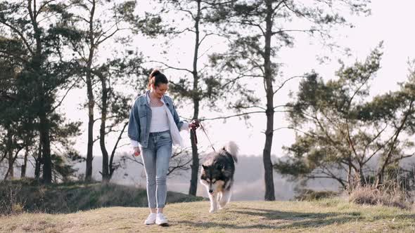 Pretty Girl Is Walking with a Cute Fluffy Dog in the Field alt