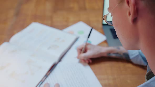 Young Man Studying at Home Writes in His Notes and Reads a Textbook alt