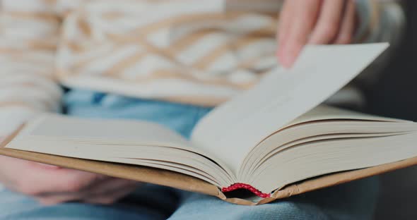 Closeup of Young Woman Reading Book in Cozy Living Room Turning Page Learning Studying Education alt