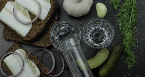 Pour Alcohol Drink Vodka From a Bottle in Two Shot Glass. Surface with Snacks alt