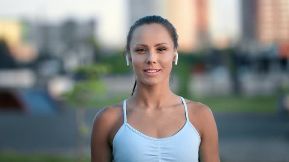 Portrait of Smiling Fitness Woman in Earphones Posing Outdoor City Street Sports Ground Cityscape alt