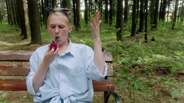 A Girl in a Blue Shirt on a Bench in the Woods Lights a Tabacco Pipe