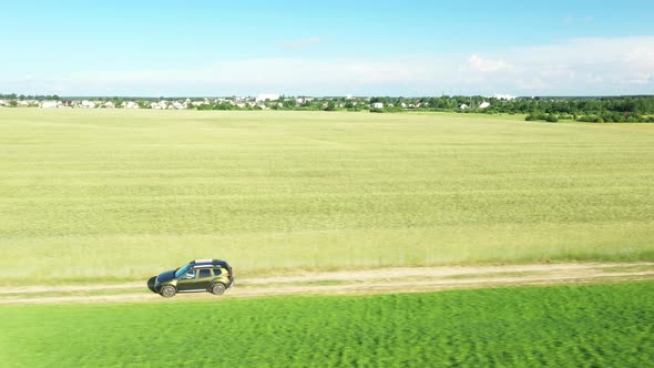 Aerial View Of Car SUV In Motion Moving On Countryside Road Through Summer Green Fields