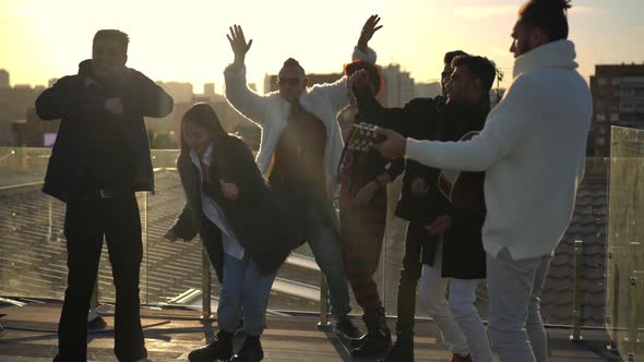 Group of Cheerful Multiethnic People Dancing at Sunset on Rooftop in Urban City alt